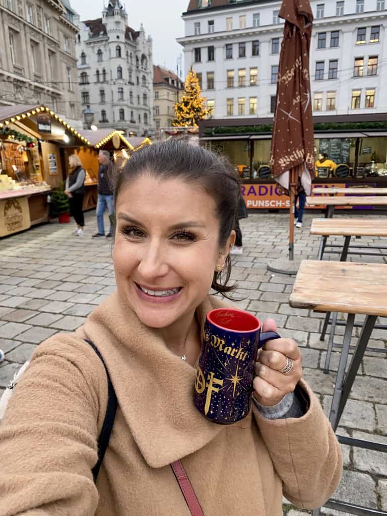 Woman enjoying a festive holiday market in Europe, holding a Christmas-themed mug.
