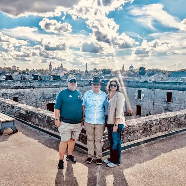 Group of three tourists standing on historic fort wall with cityscape background.