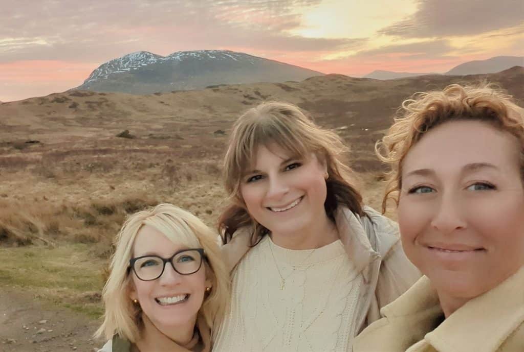 Group of three women smiling outdoors with Icelandic landscape in background.