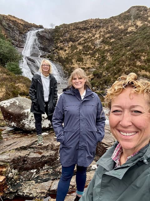 Three women enjoying a waterfall hike in outdoor gear.