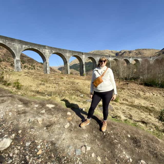 Woman standing outdoors with viaduct in background during daytime.